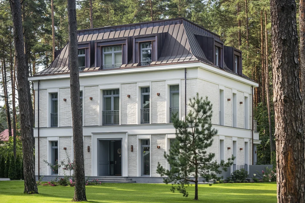 ,Dviejų aukštų klasikinės architektūros namas su mansardiniu stogu tarp Valakampių pušų.