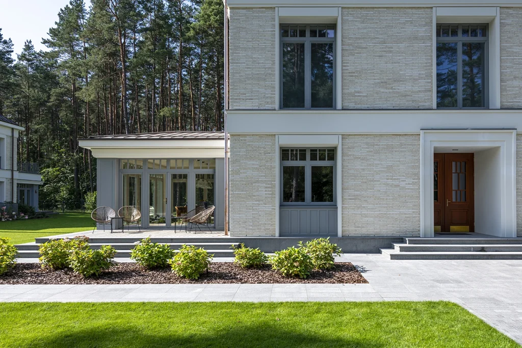 Klasikinio namo šviesaus plytų fasado detalės, simetriški langai ir dekoratyviniai šviestuvai.